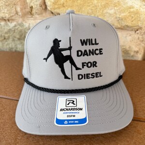 May include: A light gray baseball cap featuring a black embroidered graphic of a person dancing on a pole with the text WILL DANCE FOR DIESEL. The cap has a black braided cord across the base of the crown and a white Richardson OSFM sticker.