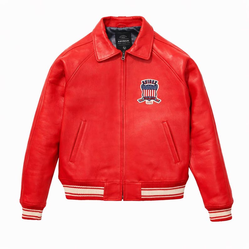 Puede incluir: Una chaqueta de cuero rojo brillante con cuello cl&aacute;sico, cremallera frontal completa y pu&ntilde;os y dobladillo acanalados con rayas blancas. Un parche en el pecho izquierdo muestra el texto AVIREX sobre un gr&aacute;fico de escudo con dise&ntilde;o de bandera.