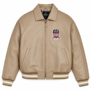 May include: A tan leather bomber jacket with a front zipper closure, a pointed collar, and ribbed cuffs and hem featuring white stripes. A patch on the left chest displays the text AVIREX above a shield with red, white, and blue flag details.