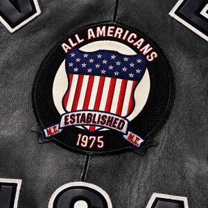 May include: A black leather jacket featuring a circular embroidered patch. The patch displays the text ALL AMERICANS, ESTABLISHED 1975, and M.C. surrounding a shield with a blue field of white stars above red and white vertical stripes.