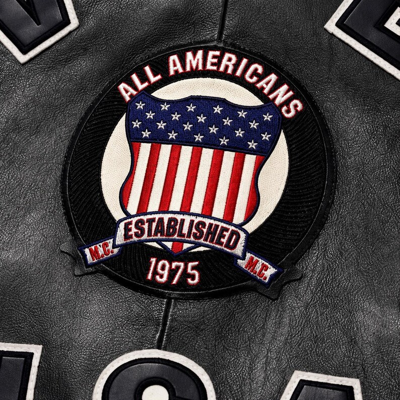 May include: A black leather jacket featuring a circular embroidered patch. The patch displays the text ALL AMERICANS, ESTABLISHED 1975, and M.C. surrounding a shield with a blue field of white stars above red and white vertical stripes.