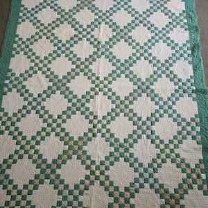 May include: A rectangular quilt featuring a repeating pattern of white fabric squares and small, multi-colored floral print squares arranged in a grid. The quilt is bordered by a solid green fabric edge and displays intricate, circular machine-stitched quilting patterns throughout the white sections.