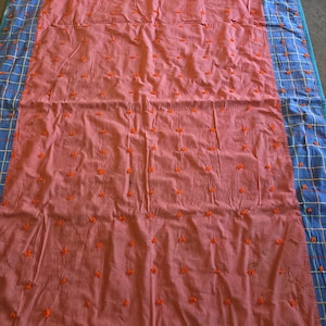 May include: A rectangular quilt featuring a large central panel of solid salmon pink fabric decorated with a grid of small, raised orange tufted accents. The quilt is bordered on the left and right sides by blue fabric with a yellow and white grid pattern.
