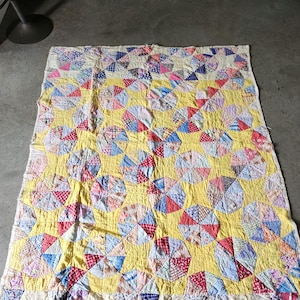 May include: A rectangular quilt featuring a repeating pattern of circular motifs composed of multi-colored fabric scraps in shades of red, blue, and white. The circular shapes are set against a bright yellow background with visible stitching.