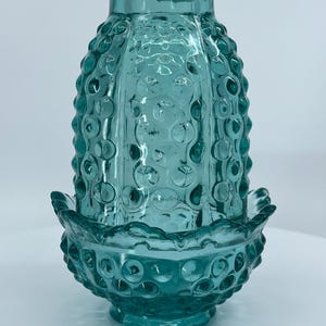 May include: A teal blue glass lamp shade featuring a hobnail pattern with raised circular bumps. The shade has a cylindrical top section and a wider, scalloped base with a matching hobnail texture throughout the entire translucent glass surface.