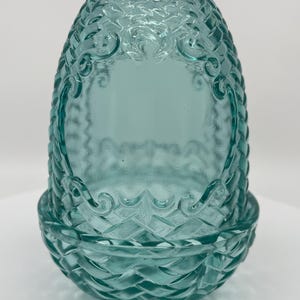 Op de afbeelding: Een doorschijnende, blauwgroene glazen lampenkap met een verhoogde mandvlechttextuur en sierlijke kruldetails. De kap heeft een afgeronde, bolvormige vorm met een brede opening aan de bovenkant en een licht uitlopende basis.