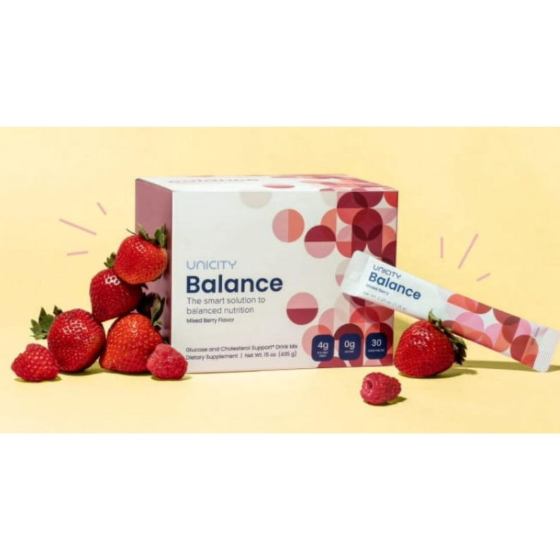 Puede incluir: Una caja y un sobre de suplemento diet&eacute;tico Unicity Balance con sabor a frutos rojos. La caja y el sobre tienen un dise&ntilde;o blanco y rojo. Fresas y frambuesas frescas est&aacute;n esparcidas alrededor de la caja y el sobre.