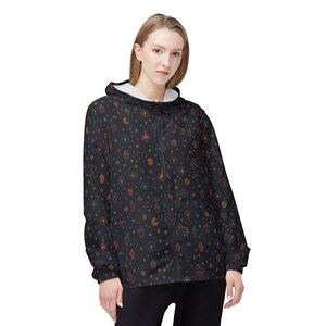 May include: Black zip-up hooded jacket with a whimsical pattern of colorful stars, hearts, rockets, and unicorns. The jacket has a white interior lining and a drawstring hood. The design is a repeating pattern of small, hand-drawn style illustrations.