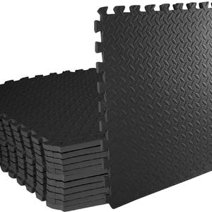 May include: A stack of square black foam floor tiles featuring an interlocking puzzle-piece edge design. Each tile has a textured diamond plate pattern on the surface, providing a non-slip finish for modular flooring applications in various spaces.