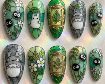 May include: A set of ten press-on nails featuring stained glass-inspired designs. The artwork includes grey creatures, black soot sprites, white flowers, green leaves, and gold-toned frames, all rendered with dark outlines on a vibrant green background.