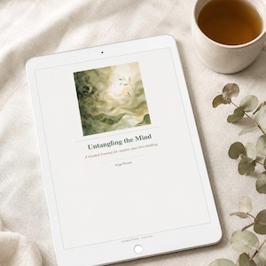 May include: A white tablet displays the cover of a guided journal titled "Untangling the Mind" with a watercolor design in green and gold. A cup of tea and eucalyptus sprigs are next to the tablet on a neutral-toned surface.