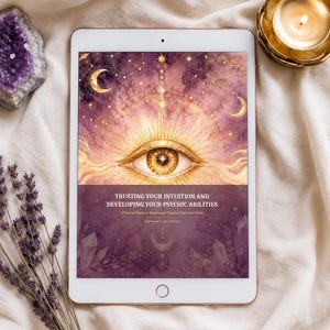 May include: A white tablet displays a book cover with an eye illustration, celestial elements, and the text "Trusting Your Intuition and Developing Your Psychic Abilities." A lit candle in a gold holder, amethyst, and lavender sprigs are also present.