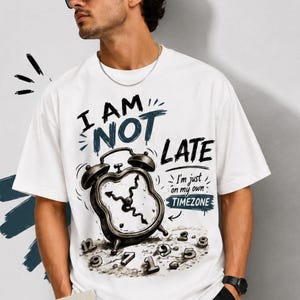 May include: A white t-shirt featuring a graphic of a distorted alarm clock with wavy hands. The text reads I AM NOT LATE, I'm just on my own TIMEZONE, and Different clock, different life. Scattered numbers surround the clock base in a dark ink style.