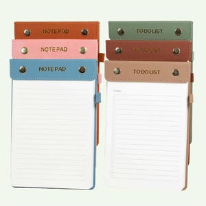 May include: A collection of six vertical rectangular notepads with coloured faux leather covers. Three are labelled NOTE PAD in blue, pink, and orange, while three are labelled TO DO LIST in green, brown, and beige. Each features metal snap buttons.
