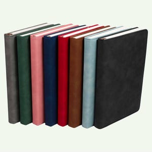 May include: A collection of eight rectangular notebooks arranged in a row, featuring solid-colored covers in shades of gray, dark green, pink, navy blue, red, brown, light blue, and black, each with a smooth texture and white page edges.