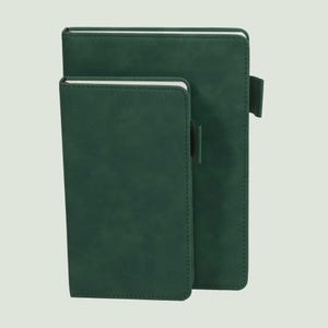 May include: Two dark green notebooks with a smooth, matte finish and rounded corners. Each notebook features a vertical elastic pen loop attached to the side. The covers are solid dark green, and the white pages are visible along the top edge.