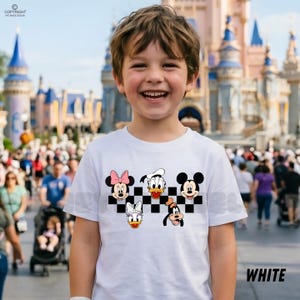 以下が含まれることがあります： 白のTシャツ。ミニーマウス、ドナルドダック、ミッキーマウス、デイジーダック、グーフィーの漫画のキャラクターが、白と黒の市松模様に描かれています。「WHITE」の文字が右下に白で印刷されています。