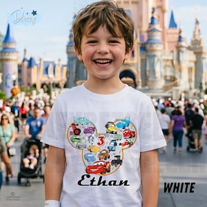 May include: A white t-shirt with a colourful graphic of cartoon cars in a Mickey Mouse head shape. The shirt has the name "Ethan" and the number "3". The word "WHITE" is printed on the bottom right.