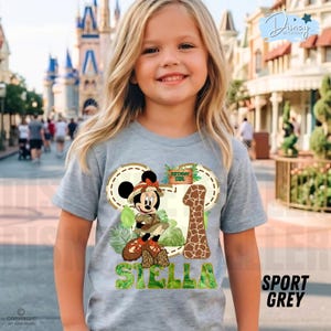 May include: A grey t-shirt with a Minnie Mouse safari design. The design includes the number 1 in a giraffe pattern, the name "Stella", and the words "Birthday Girl". The shirt is labelled "Sport Grey".