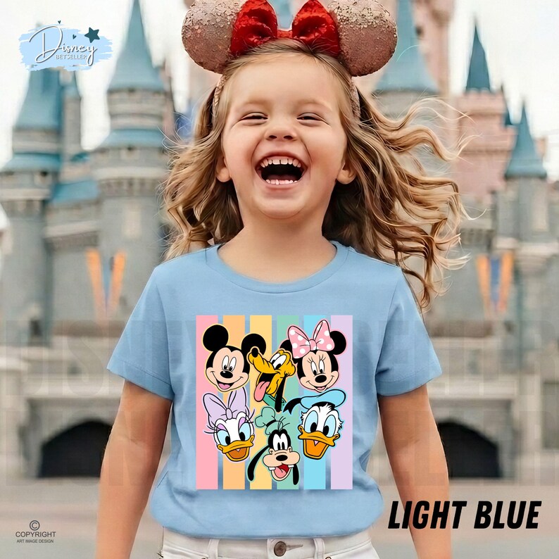 May include: A light blue t-shirt featuring a colorful graphic of Mickey Mouse, Minnie Mouse, Donald Duck, Daisy Duck, Goofy, and Pluto. The shirt has the text "LIGHT BLUE" at the bottom. The child is wearing a Minnie Mouse ear headband.