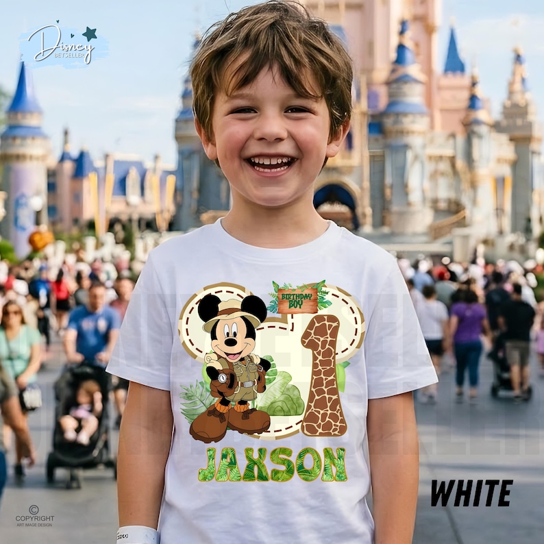 May include: White t-shirt with a Mickey Mouse safari design, the text "Birthday Boy", and the number "1". The name "Jaxson" is printed in green. The shirt is a birthday theme.
