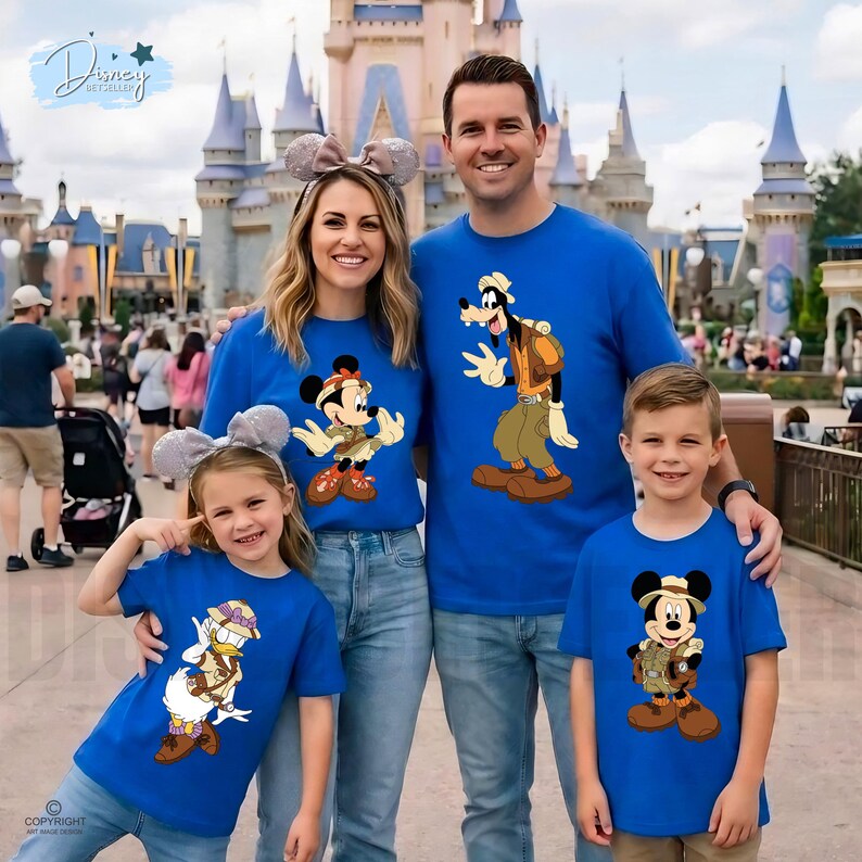 May include: A group of four people wearing matching royal blue t-shirts featuring Disney characters dressed in safari gear. The shirts display illustrations of Mickey Mouse, Goofy, Donald Duck, and Mickey Mouse again, all wearing hats and vests.