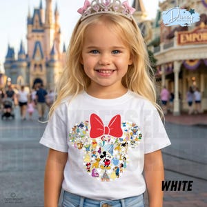 May include: A young girl wearing a white t-shirt featuring a Minnie Mouse design. The design includes a large red bow and various Disney characters. The girl is also wearing a pink tiara. The word "WHITE" is printed on the shirt.