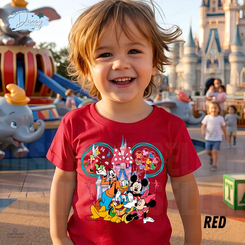 May include: A red t-shirt with a Disney-themed graphic featuring Mickey and Minnie Mouse, Goofy, and Donald Duck. The design includes a castle and balloons. The shirt is worn by a child in an outdoor setting.