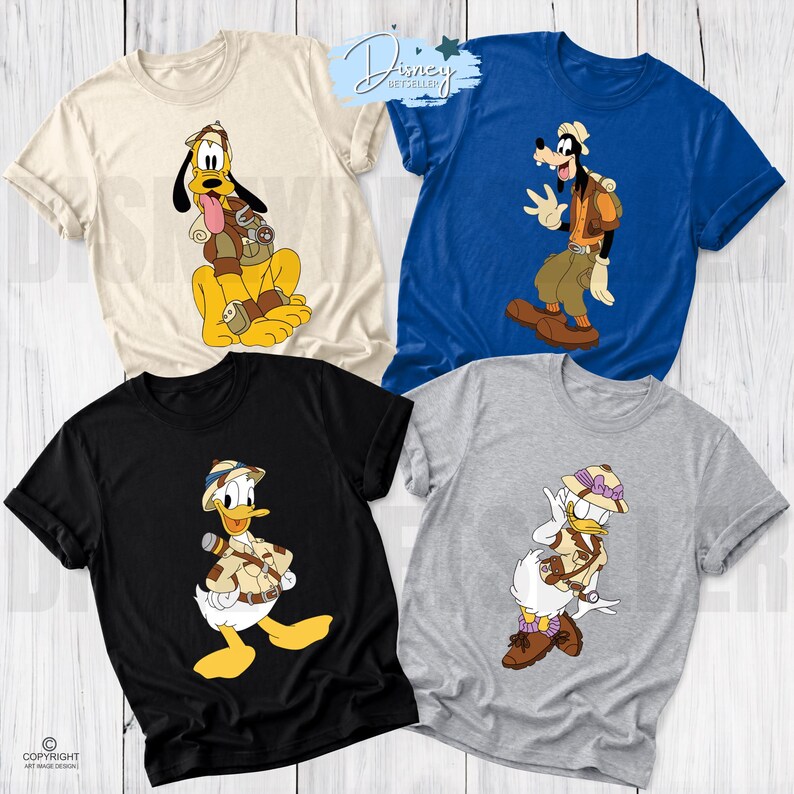 May include: Four short-sleeve t-shirts in cream, blue, black, and gray. Each shirt features a Disney character dressed in safari gear: Pluto, Goofy, Donald Duck, and Daisy Duck. The characters wear pith helmets and carry backpacks or gear.