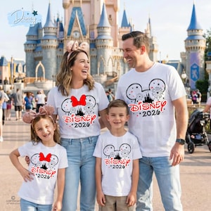 May include: A family of four wearing matching white t-shirts with a Disney design. The design includes Mickey Mouse ears, fireworks, and the text "DISNEY *2026". The family is smiling in front of a castle.