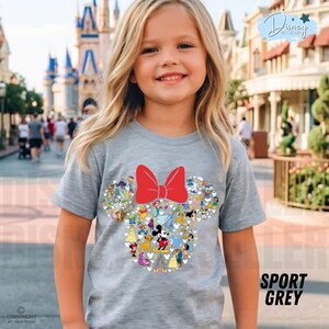 May include: A light gray t-shirt featuring a Minnie Mouse design made up of various Disney characters and a large red bow. The shirt has the words "SPORT GREY" printed on the bottom right.