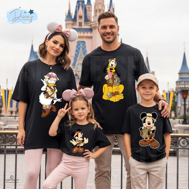 May include: Four black short-sleeved t-shirts featuring Disney characters in safari gear. One shirt displays Daisy Duck, one shows Pluto, one features Minnie Mouse, and one depicts Mickey Mouse. Each character wears a tan hat and vest.
