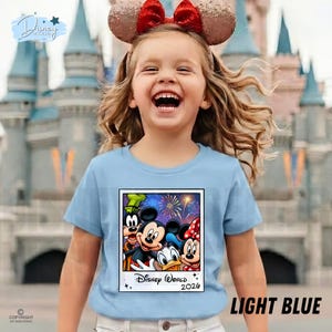 Puede incluir: Una camiseta azul claro con un gr&aacute;fico de Mickey Mouse, Minnie Mouse, Donald Duck y Goofy con fuegos artificiales y el texto "Disney World 2026". La camiseta la lleva un ni&ntilde;o que lleva una diadema con orejas de Minnie Mouse.