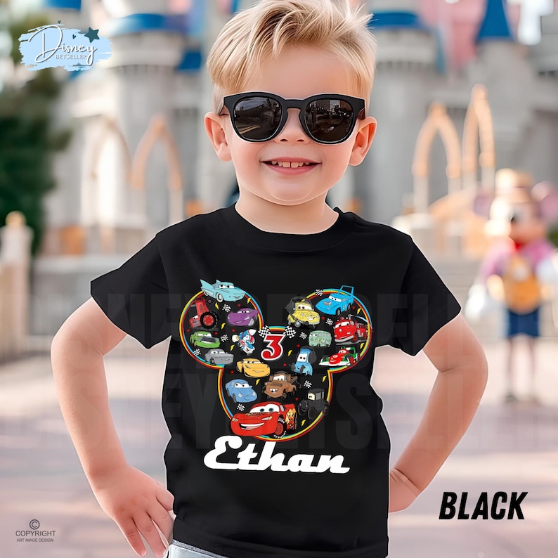 May include: Black t-shirt with a Mickey Mouse-shaped design filled with cartoon cars. The number "3" is displayed, along with the name "Ethan" in white. The word "BLACK" is printed on the lower right.