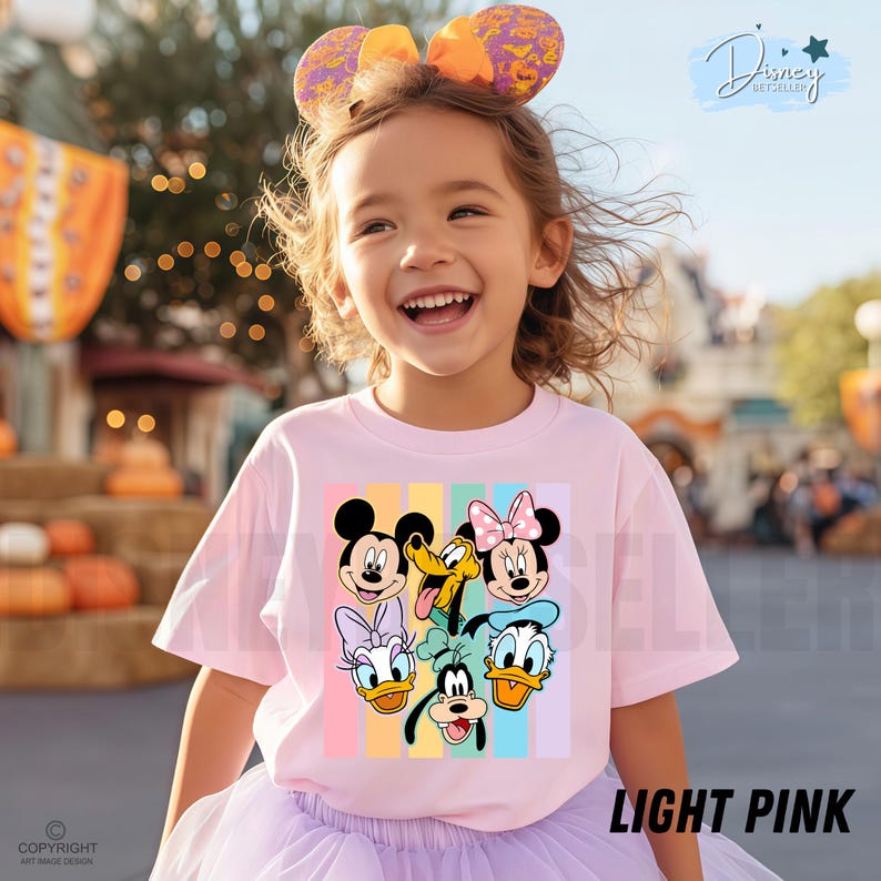 May include: A light pink t-shirt featuring a colorful graphic of Disney characters, including Mickey Mouse, Minnie Mouse, Donald Duck, and Goofy. The shirt has a crew neck and short sleeves. The text "LIGHT PINK" is at the bottom right.