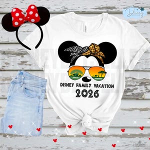 May include: White t-shirt with a Minnie Mouse graphic wearing sunglasses with an Animal Kingdom design. The text "Disney Family Vacation 2026" is printed below the graphic. A red and white polka dot bow headband and blue jeans are also in the image.