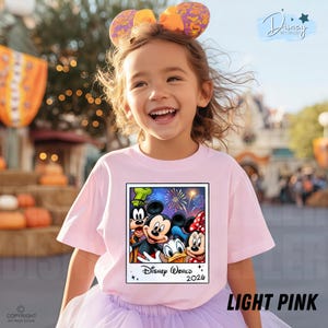 Puede incluir: Una camiseta rosa claro con un gr&aacute;fico de Mickey Mouse, Minnie Mouse, Donald Duck y Goofy. El gr&aacute;fico est&aacute; enmarcado como una foto Polaroid e incluye el texto "Disney World 2026". La camiseta la lleva un ni&ntilde;o sonriente.