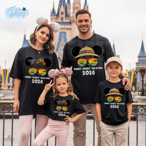 May include: A family of four wearing matching black t-shirts with a Mickey Mouse design and the text "Disney Family Vacation 2026." The design includes sunglasses and a safari hat. The background shows a castle.