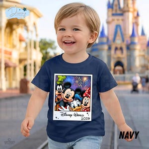 Puede incluir: Camiseta azul marino con un gr&aacute;fico de Mickey Mouse, Minnie Mouse, Donald Duck y Goofy, con fuegos artificiales y el texto "Disney World 2026". La camiseta la lleva un ni&ntilde;o sonriente.