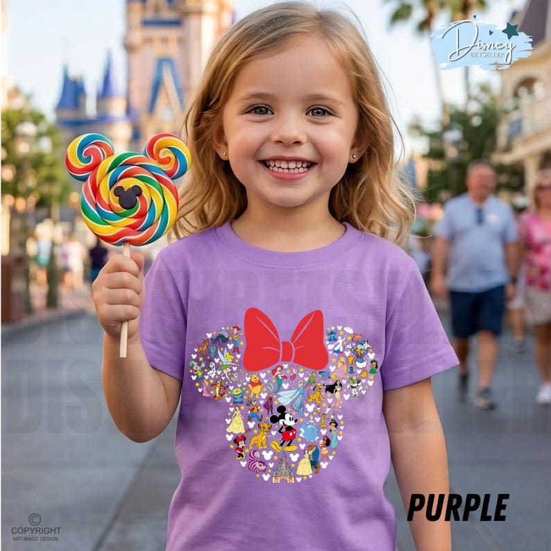 May include: A young girl smiles, holding a colorful lollipop. She wears a purple t-shirt with a Minnie Mouse design, featuring a red bow and character illustrations. The word "PURPLE" is printed on the shirt.