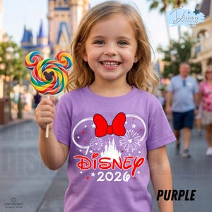 May include: A young girl smiles, holding a colorful Mickey Mouse-shaped lollipop. She wears a purple t-shirt with a red bow, fireworks, and the text "Disney 2026". The background features a Disney theme park.