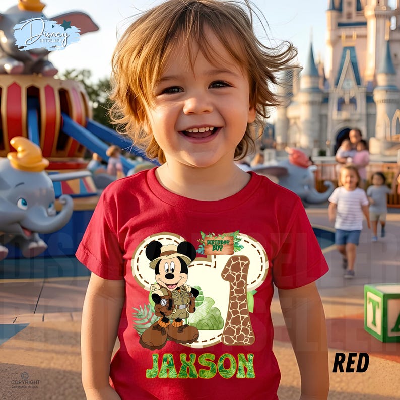 May include: A red t-shirt with a Mickey Mouse explorer design, the number 1, and the name "Jaxson". The design incorporates a giraffe pattern and the words "Birthday Boy".