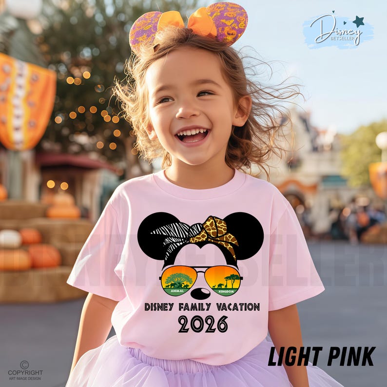 May include: A light pink t-shirt featuring a Minnie Mouse design with sunglasses and the text "Disney Family Vacation 2026". The shirt is worn by a child with a matching headband.