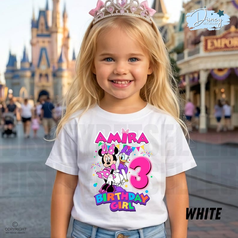 May include: A white short-sleeved t-shirt featuring a colorful graphic of Minnie Mouse and Daisy Duck, the name Amira, and a large pink number 3. The design includes festive confetti and the text Birthday Girl in bright, bold, multi-colored lettering.