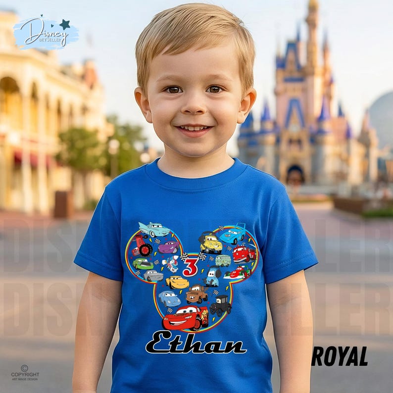 May include: A blue t-shirt with a Mickey Mouse-shaped design filled with cartoon cars. The number "3" is in the center, with the name "Ethan" below. The shirt is worn by a young child.
