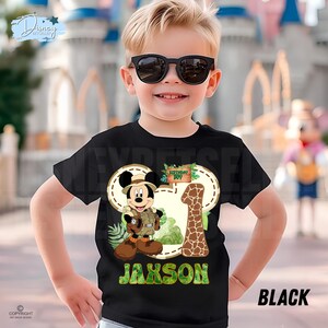May include: Black t-shirt with a Mickey Mouse safari design, a giraffe-patterned number 1, and the name "Jaxson" in green. The shirt also has the words "Birthday Boy".