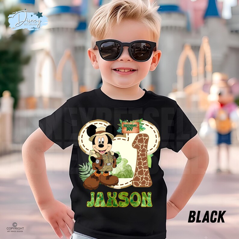 May include: Black t-shirt with a Mickey Mouse safari design, a giraffe-patterned number 1, and the name "Jaxson" in green. The shirt also has the words "Birthday Boy".