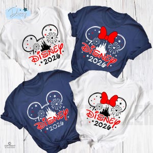 May include: Four short-sleeved t-shirts in white and navy blue. Each shirt features a Mickey Mouse head design with fireworks, a castle, and the word "Disney" in red, along with the year "2026". Two shirts have a red bow.