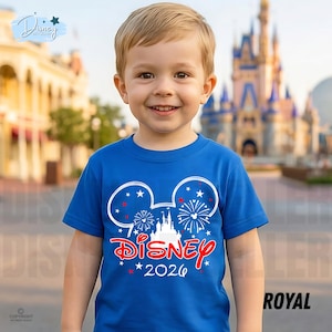 May include: A royal blue t-shirt featuring a white Mickey Mouse head design with fireworks and a castle. The word "Disney" is in red script, with "2026" below. The shirt is worn by a young child.