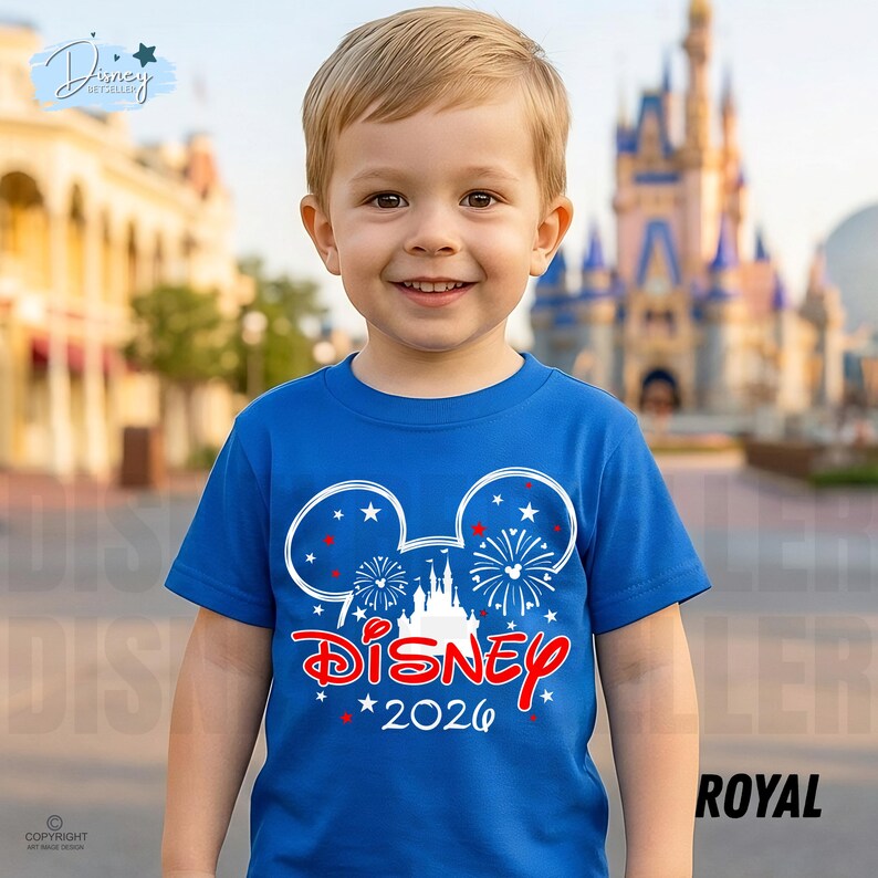May include: A royal blue t-shirt featuring a white Mickey Mouse head design with fireworks and a castle. The word "Disney" is in red script, with "2026" below. The shirt is worn by a young child.